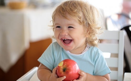 Little boy laughing and eating an apple