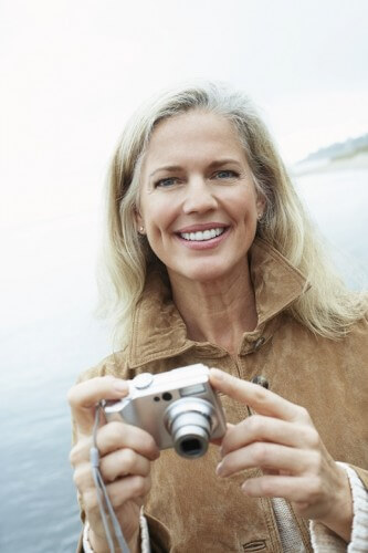 Smiling older woman at the beach holding a camera