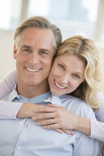 Middle age couple smiling at camera with woman back hugging man