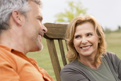 Middle age couple smiling at each other seated in a field