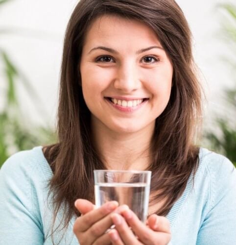 Woman smiling and holding up glass of water cupped in her hands